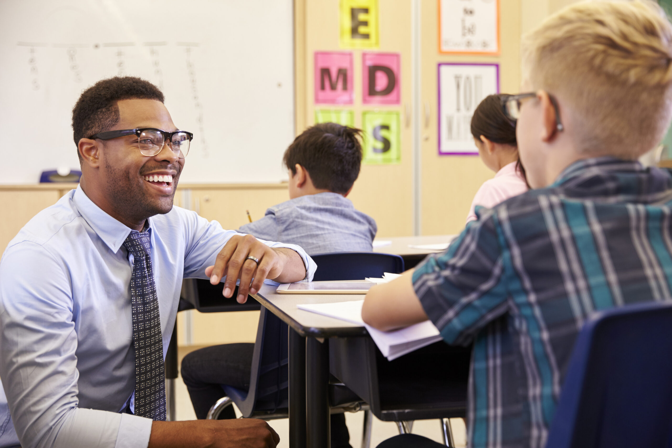 Smiling teacher kneeling beside elementary school pupilâs desk