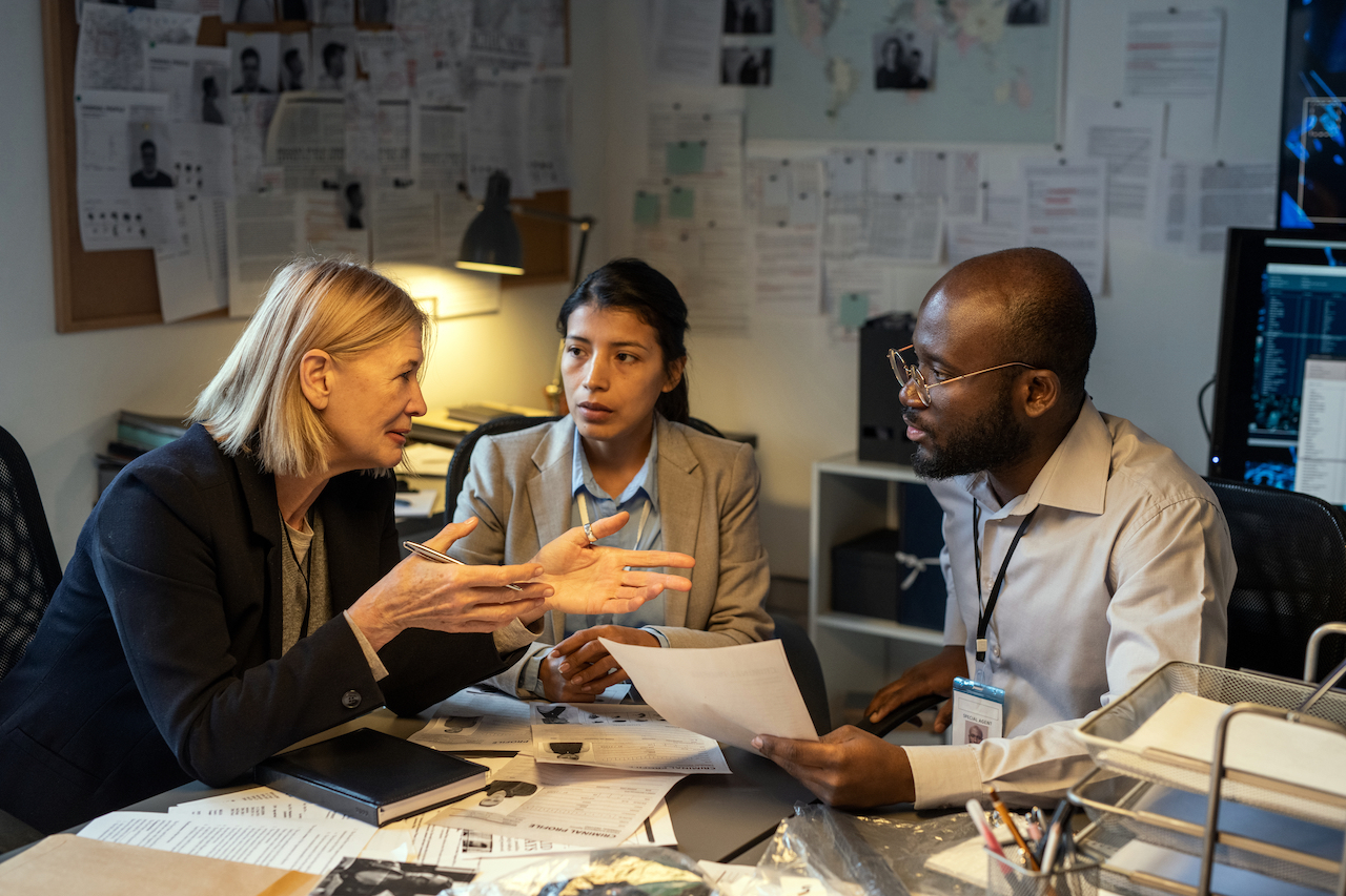 Group of confident and experienced investigators in formalwear discussing versions of murder or other crime by workplace