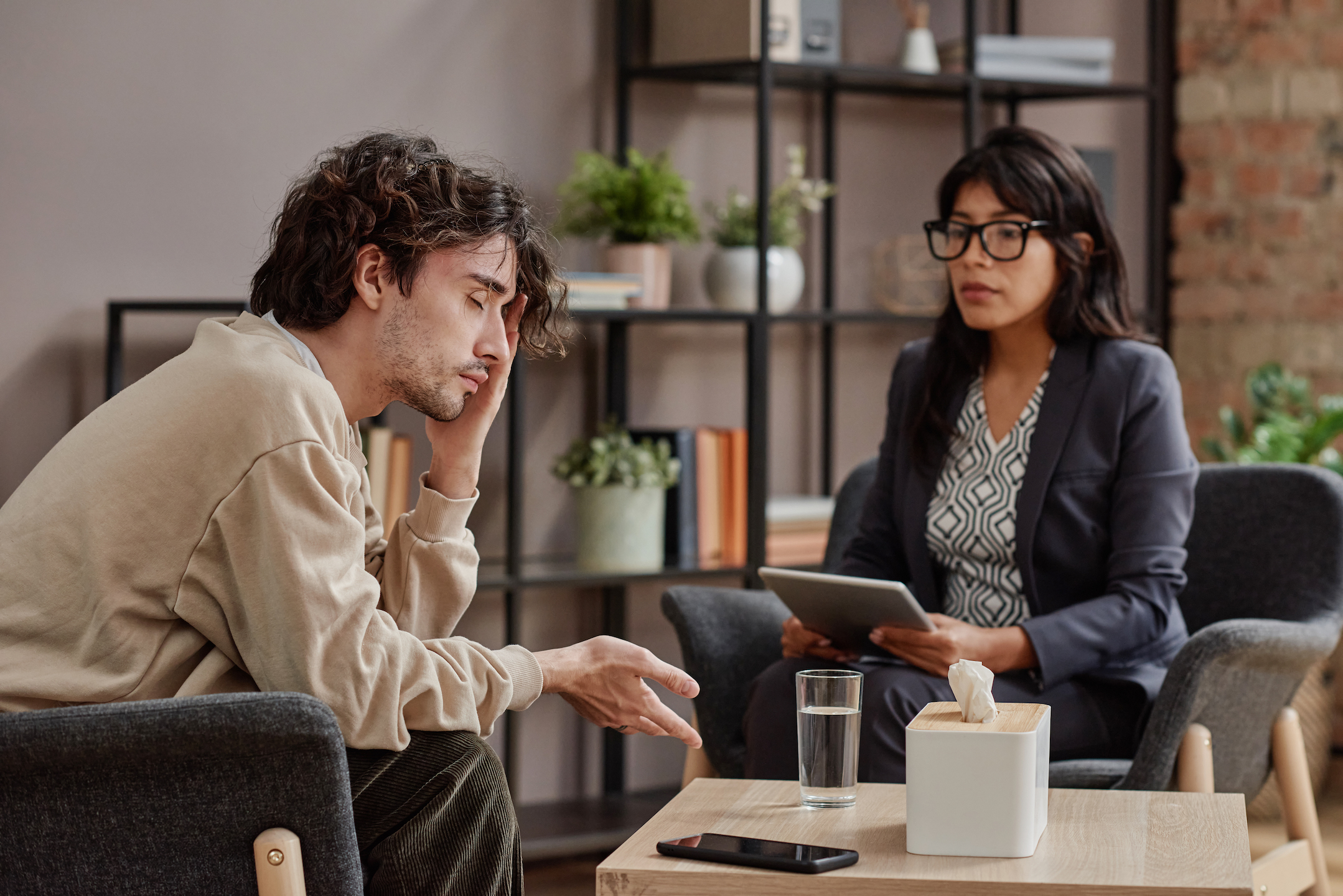 Horizontal medium shot of sad young man treating depression with help of professional psychotherapist