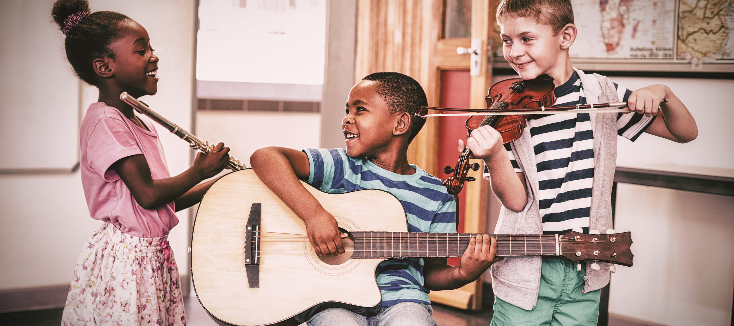 Smiling children playing musical instruments in classroom at school