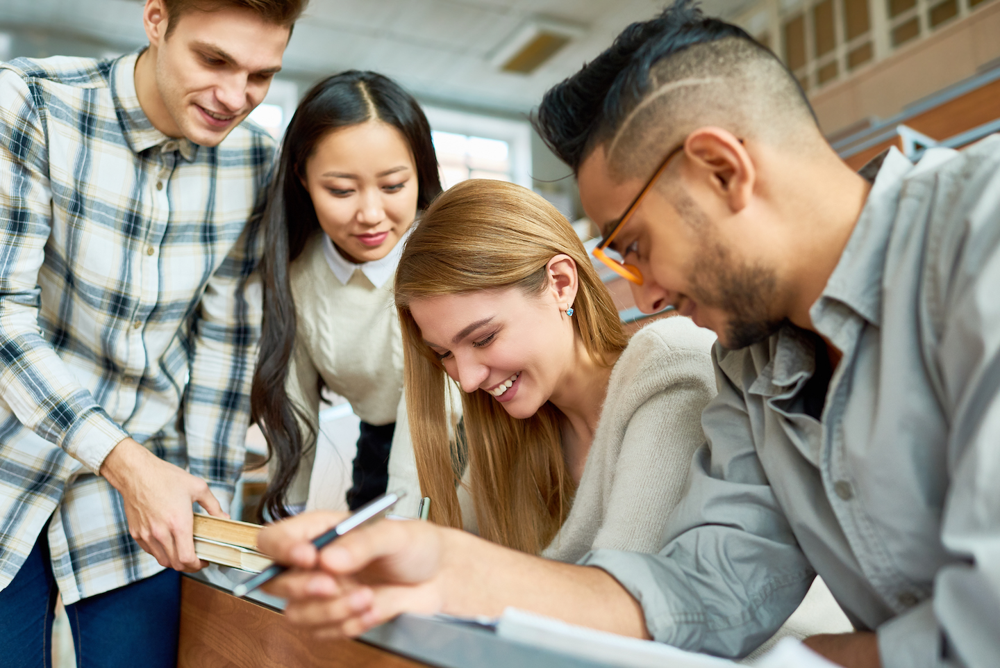 Multi-ethnic group of students having fun  and laughing  in lecture hall of modern college while enjoying classes, focus on beautiful young woman with friends