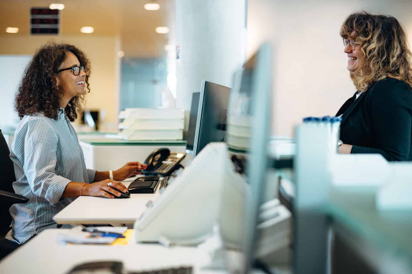 Smiling administrator talking with a woman standing at reception desk. Woman visiting municipal office for work and talking with the receptionist.