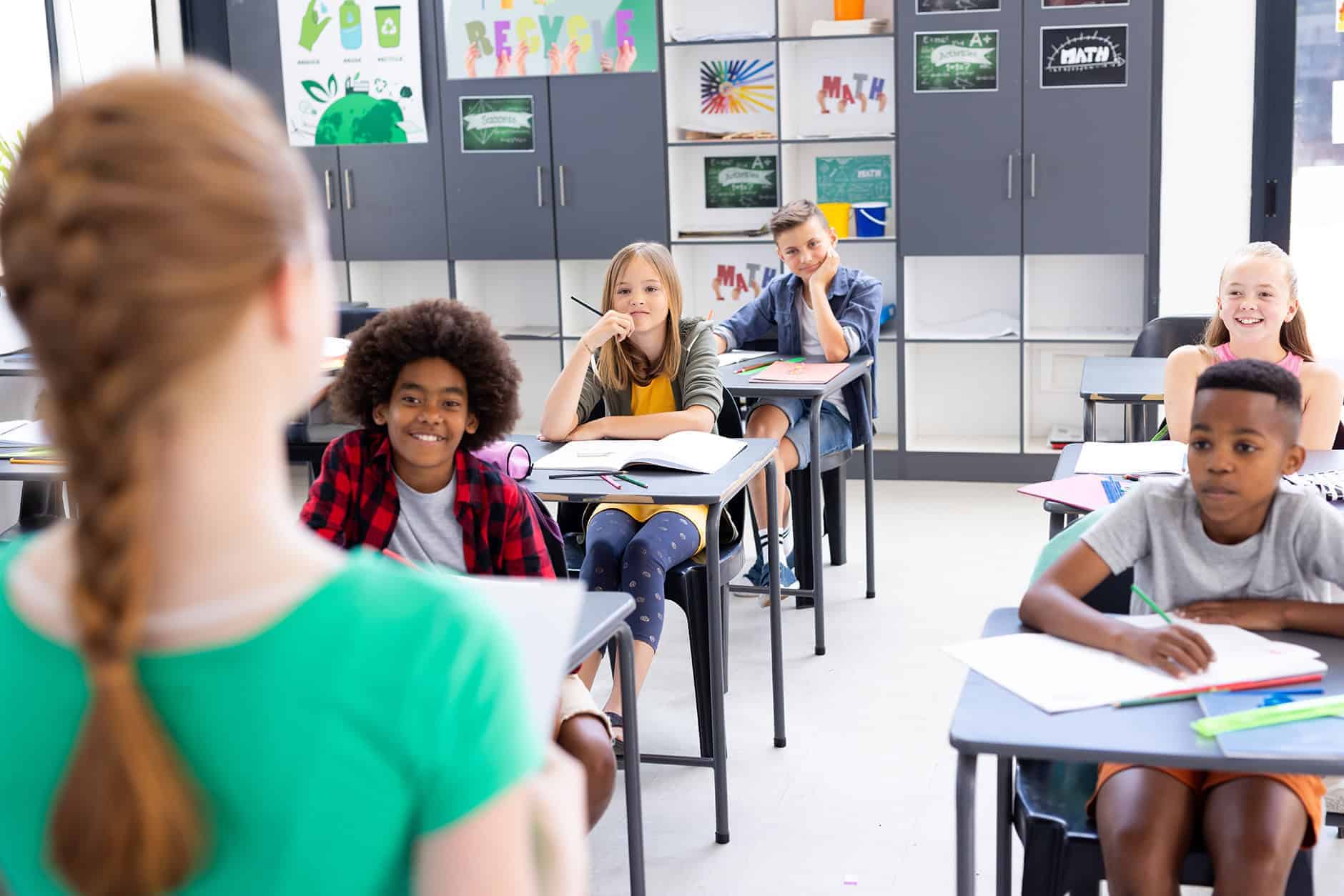 diverse-pupils-sitting-at-desks-listening-to-schoo-2023-11-27-05-06-54-utc (1)