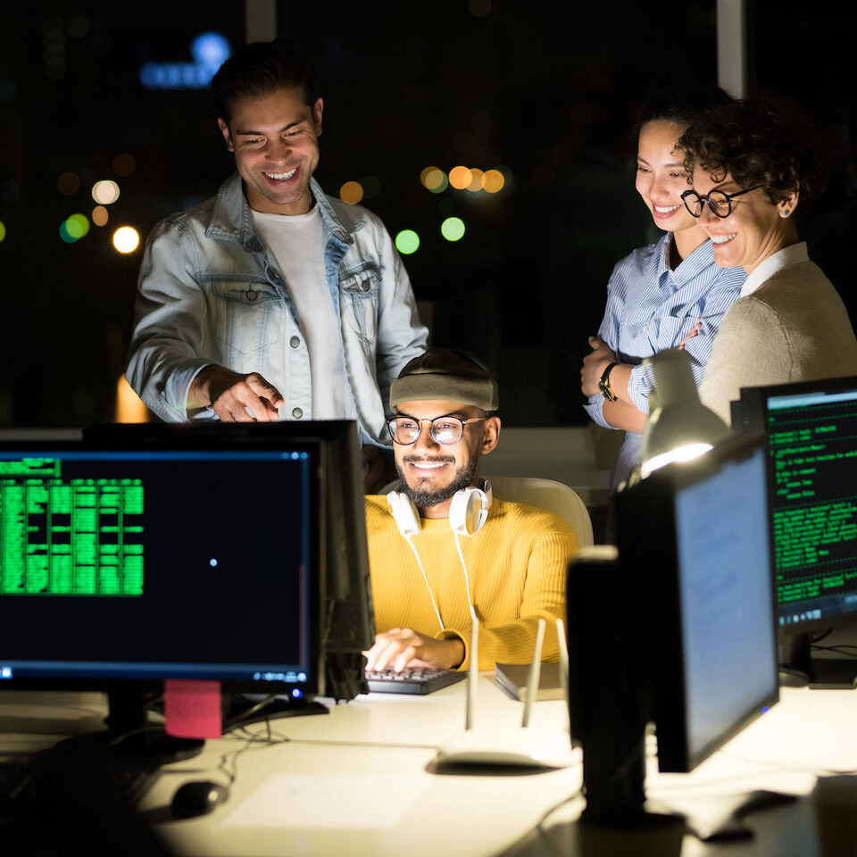 Group of excited young people standing over computer while finishing startup project at night
