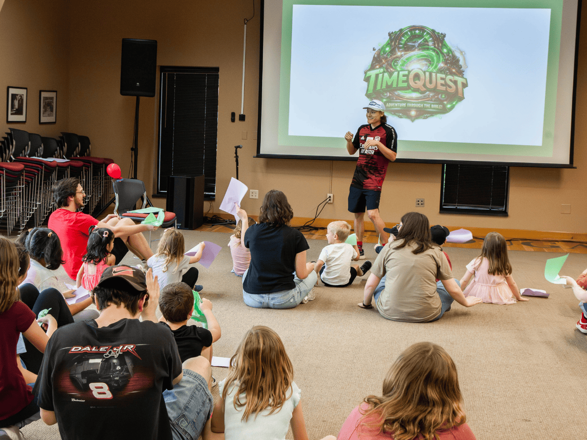 Children and adults attending a pastoral ministry event, listening to a speaker in a community room.