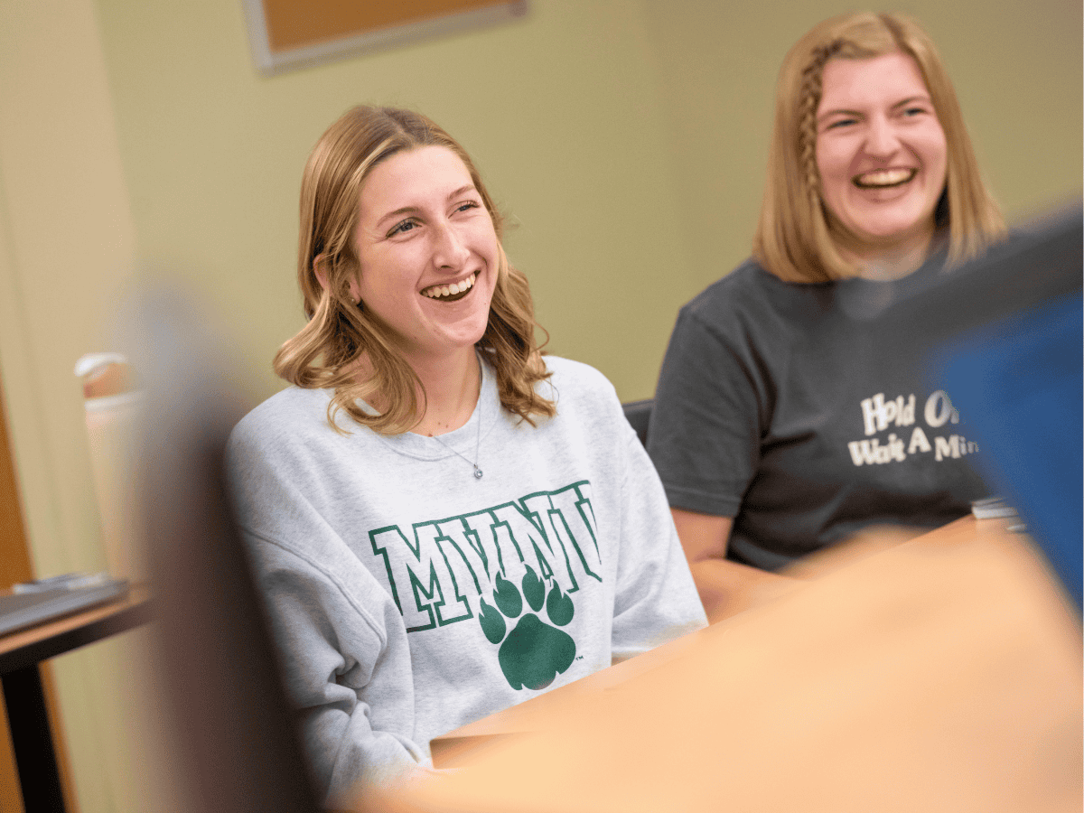 Smiling young women in a classroom, engaging in a group discussion or activity.
