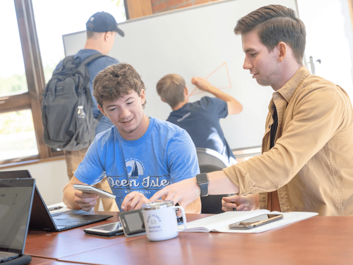Students collaborating in a classroom with laptops and tablets, engaging in a group activity.