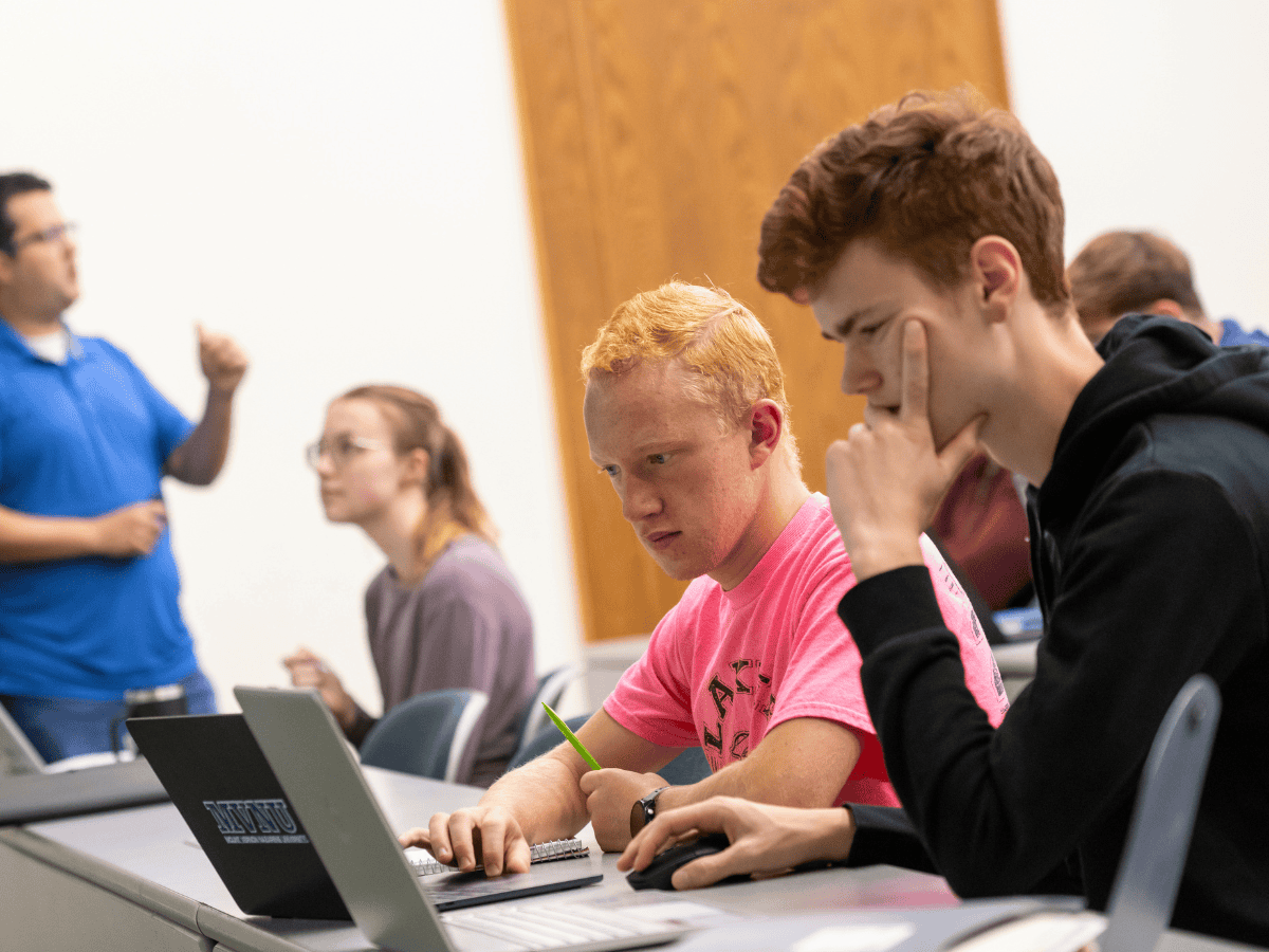 Students attentively listening and taking notes during a classroom lecture with a teacher in the bac.