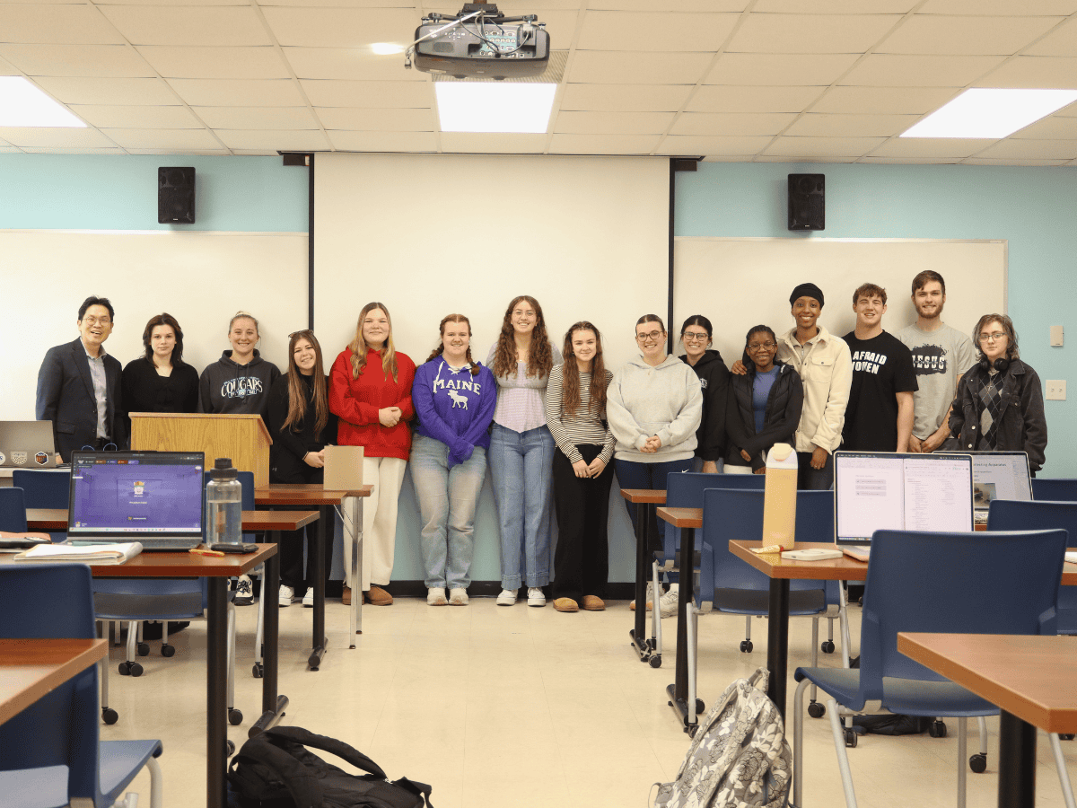 Students standing in a classroom with computers and a projector screen.