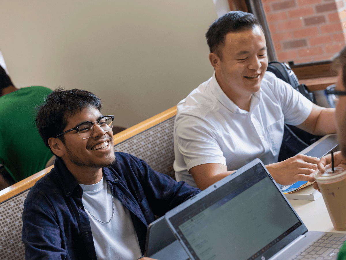 Relaxed students studying together in a classroom with laptops and coffee.