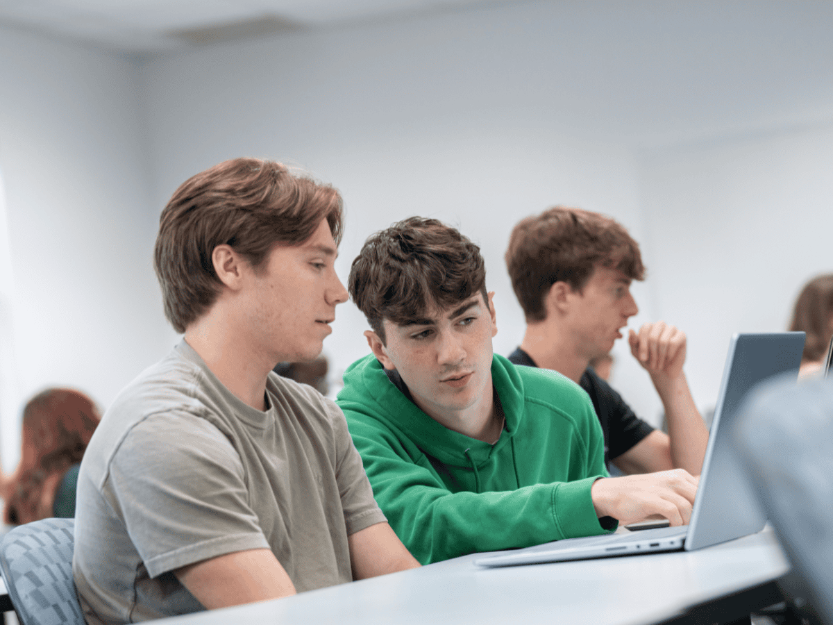 Young students studying in a classroom with laptops and attentive expressions.