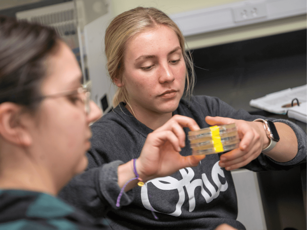 Two young women examining a small container with yellow and gray components.