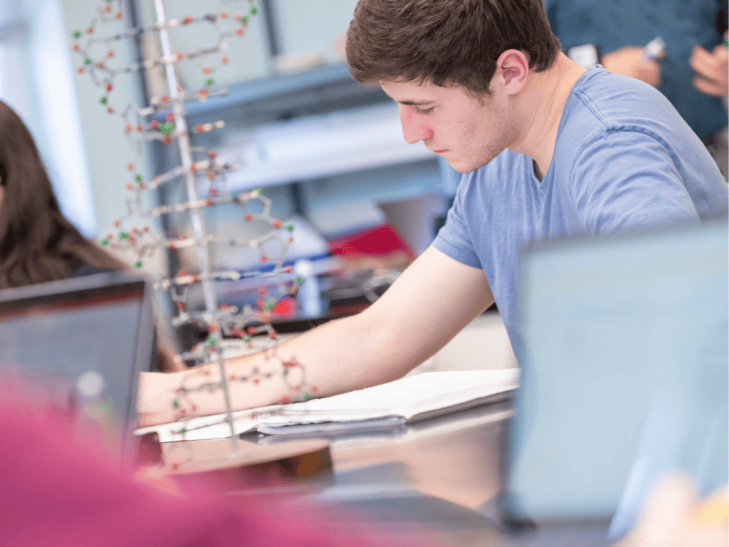 A young male student working on genetic research with DNA models in a science lab.