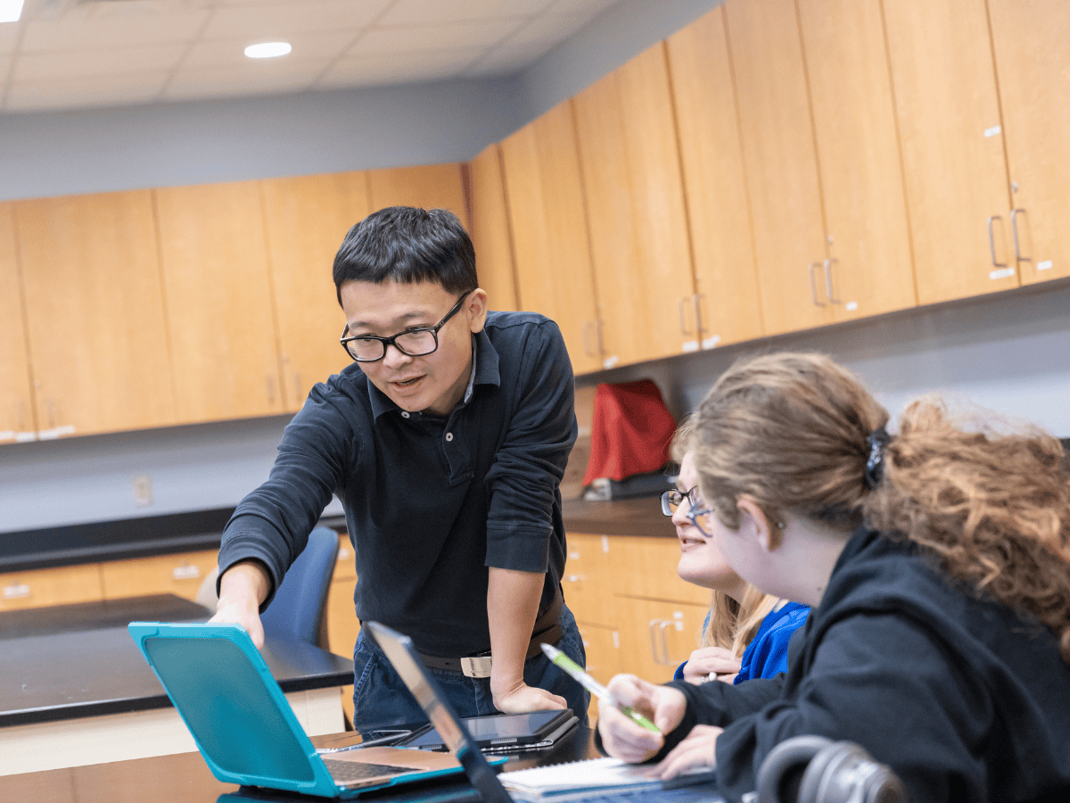 Teacher helping students with laptops during class activity.