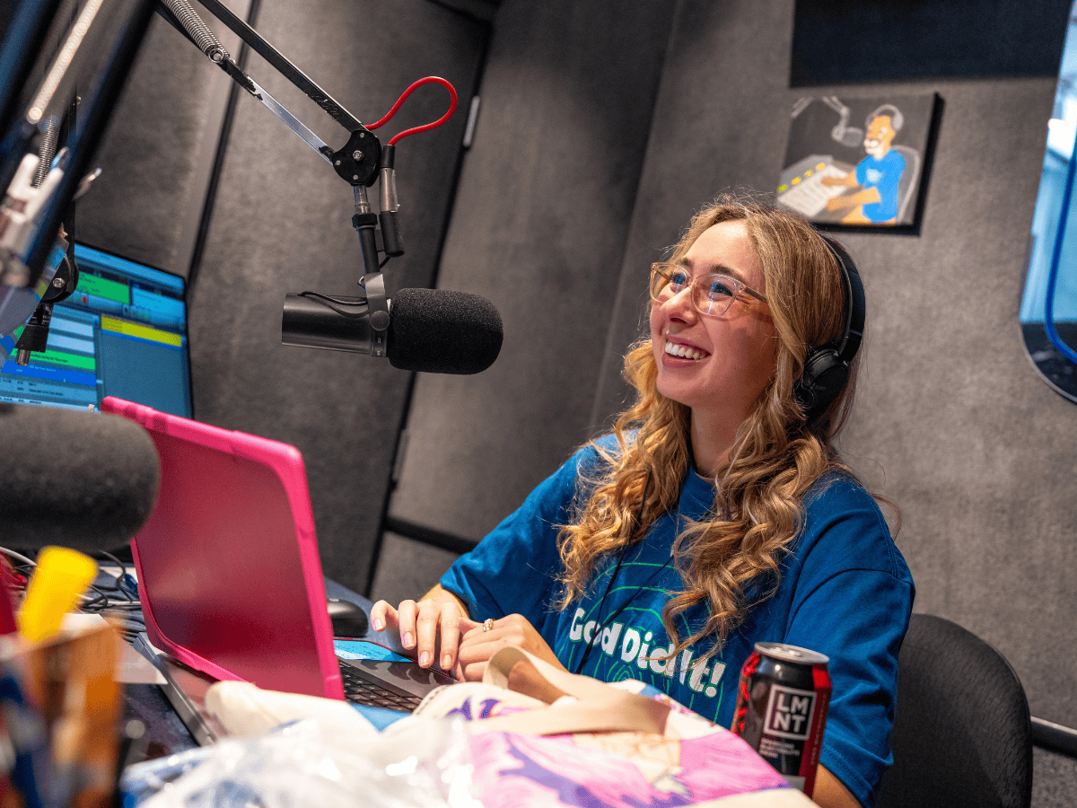 A woman wearing headphones speaking into a microphone in a radio studio.
