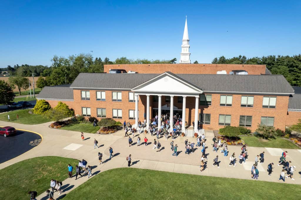 Students gathering outside a brick school building with white columns and a prominent steeple in the.