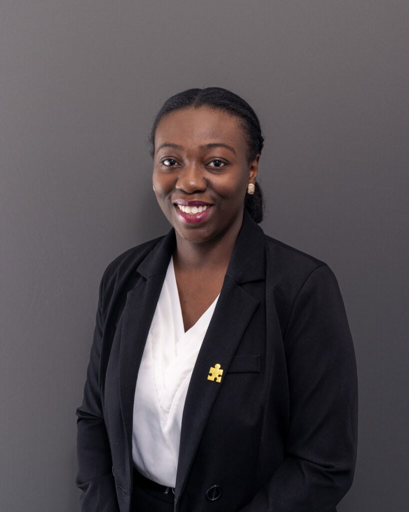 Confident African American woman in professional attire smiling against gray background.