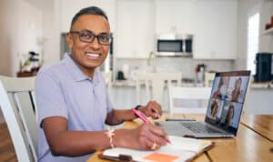 Adult student taking notes during MVNU online class on laptop.