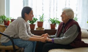 Social worker offering emotional support to elderly woman at home, symbolizing faith-based compassion and care.