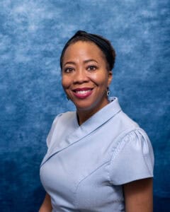 Nurse smiling in uniform against blue background.