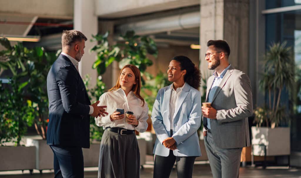 A small group of professionals talk in a bright office lobby. The image captures the spirit of collaboration and career growth highlighted in MVNU’s MSM vs. MBA blog, where online learners explore which business path best fits their goals.