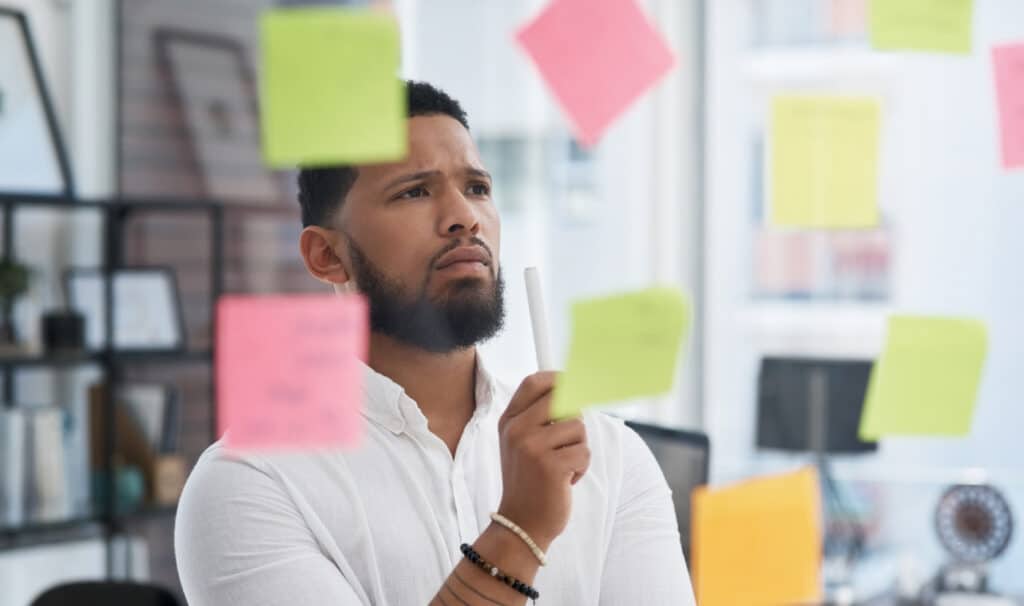 An adult learner brainstorming business ideas on a glass wall, reflecting the thoughtful process of exploring BBA majors and building leadership skills through a business degree.