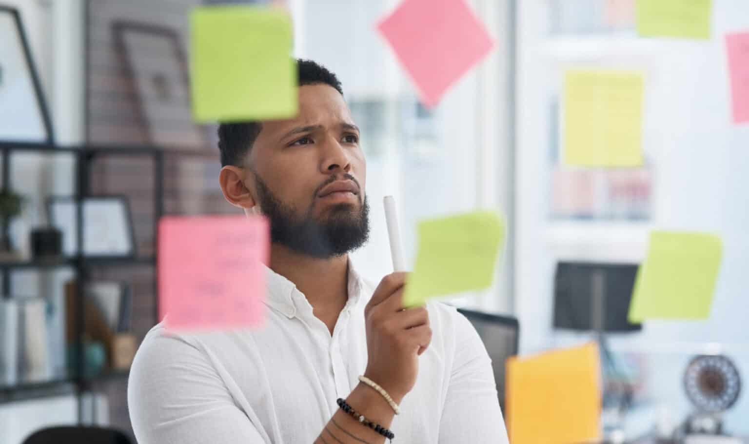 An adult learner brainstorming business ideas on a glass wall, reflecting the thoughtful process of exploring BBA majors and building leadership skills through a business degree.