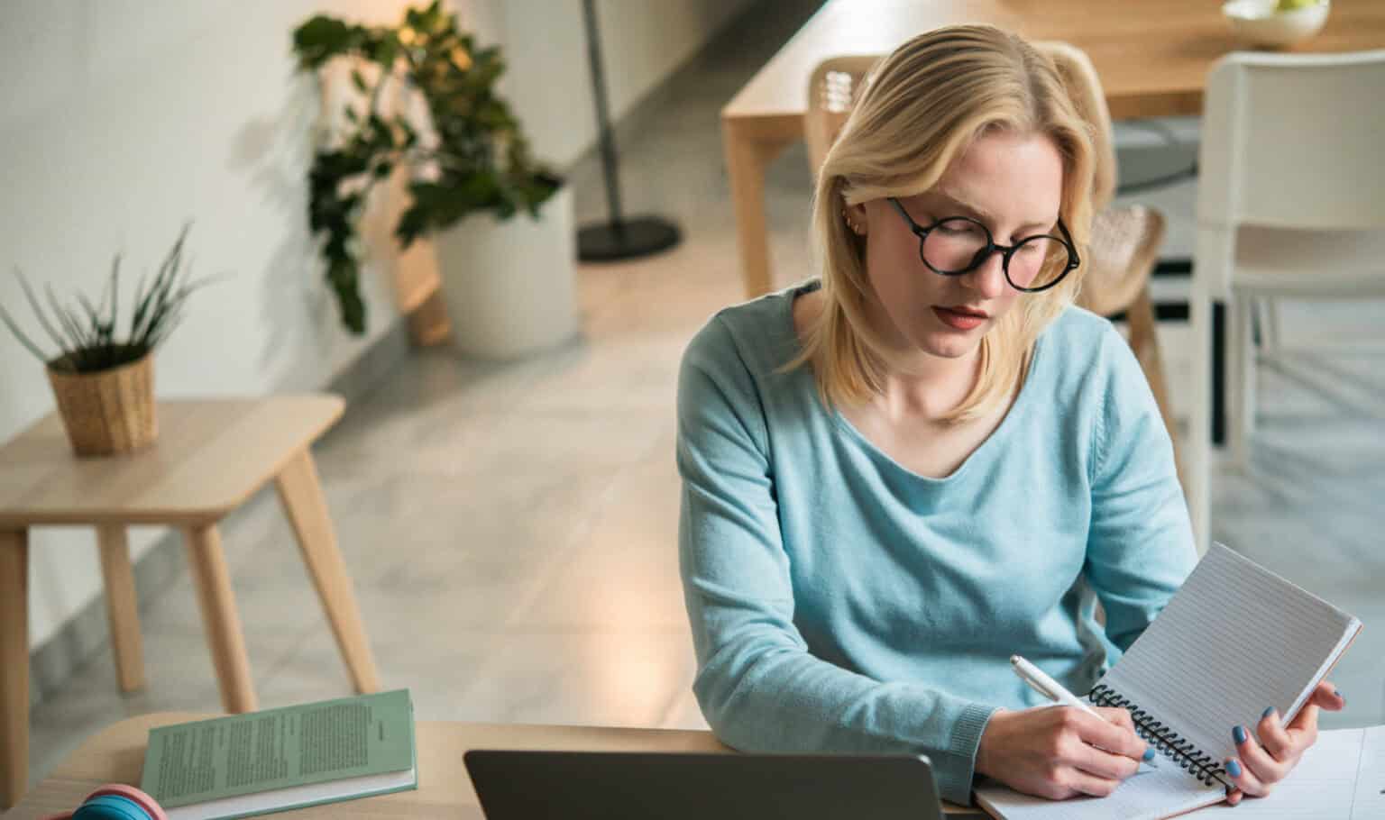 Adult learner studying online at home, taking notes beside a laptop while returning to school to pursue an associate degree