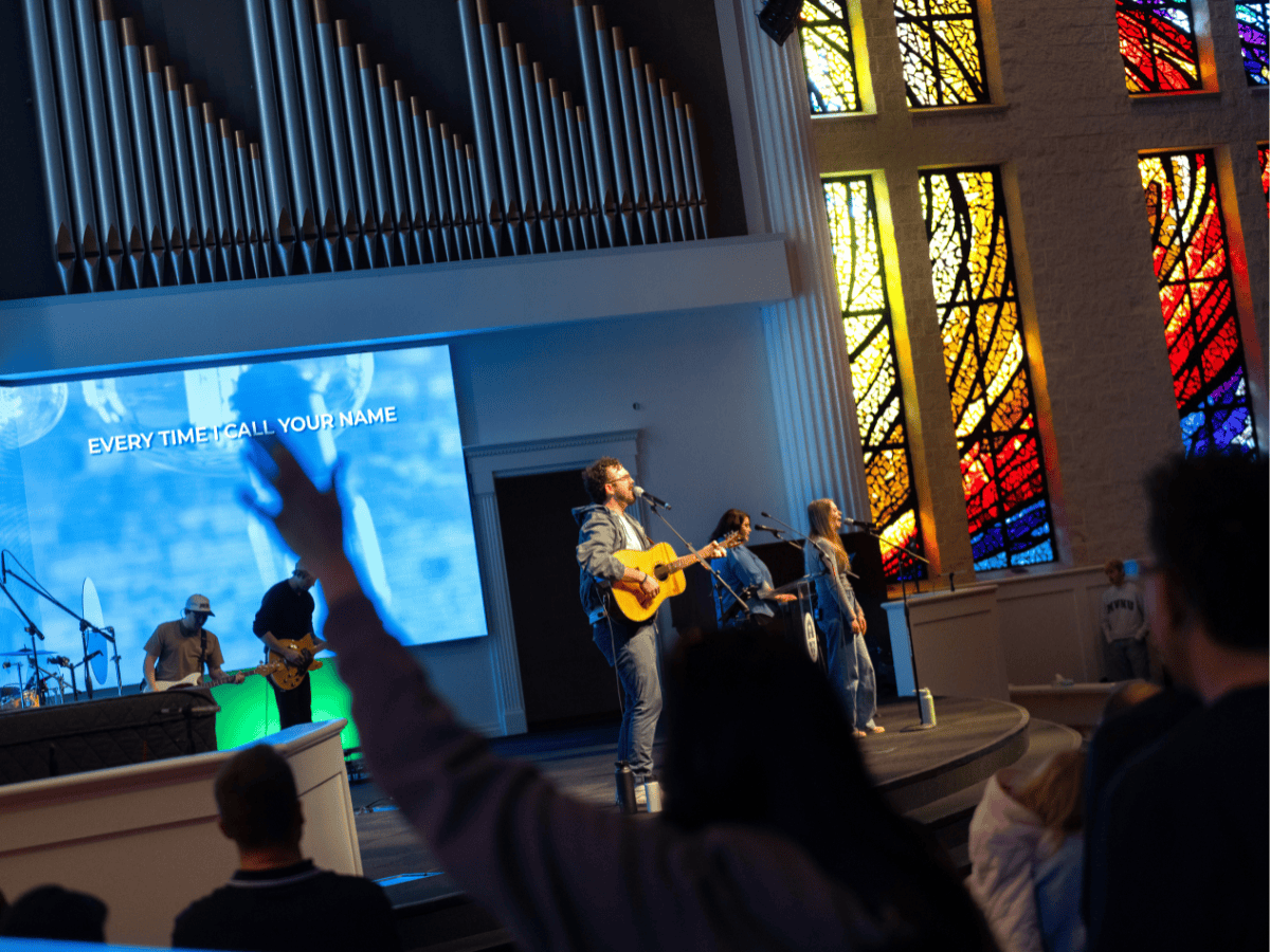 A church band performing on stage with stained glass windows in the background.