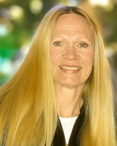 A smiling woman with long blonde hair outdoors in a park setting.