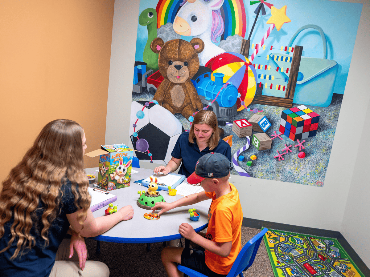 Therapist and children playing with toys in a colorful therapy room.