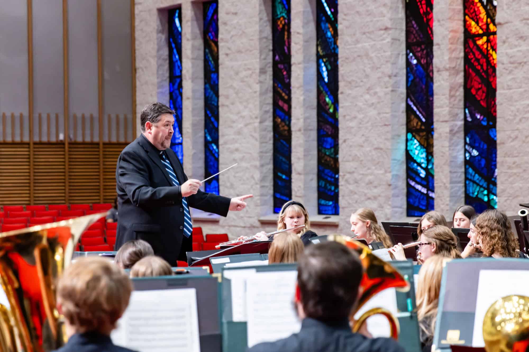 Conducting a school orchestra in a church with stained glass windows.