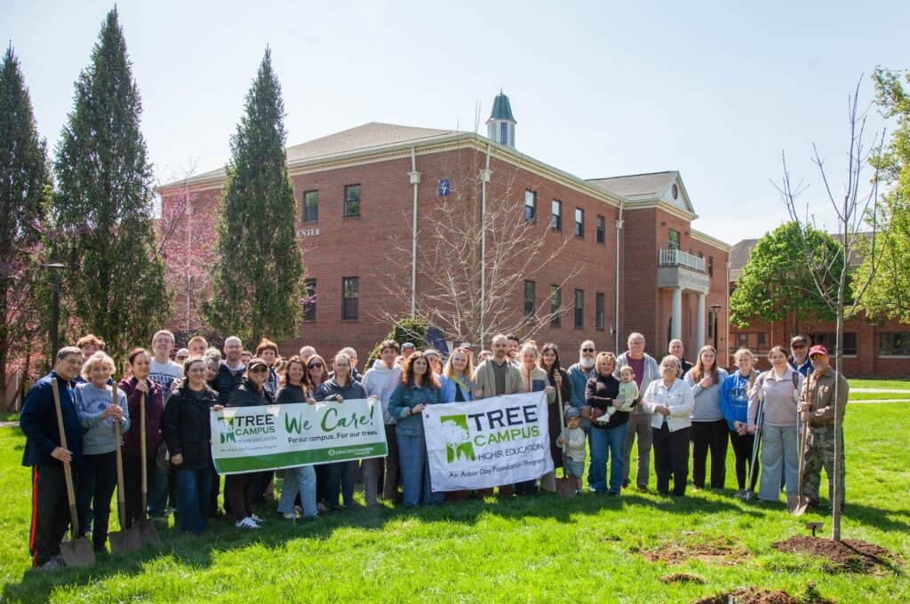 Planting community members holding banners during a tree planting event on a university campus.