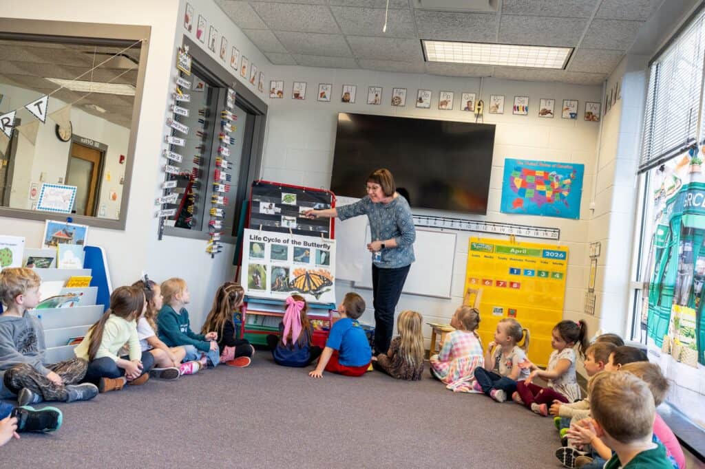Early childhood classroom with teacher and young students sitting on the carpet listening attentivel.