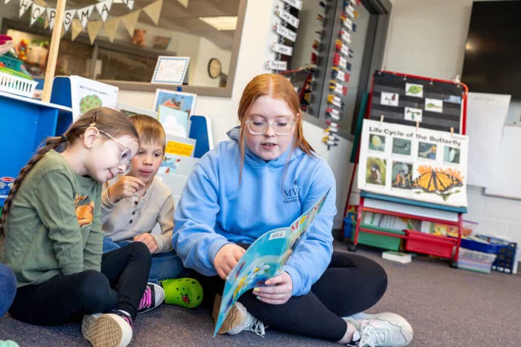Reading a children's book in a classroom library with young students.