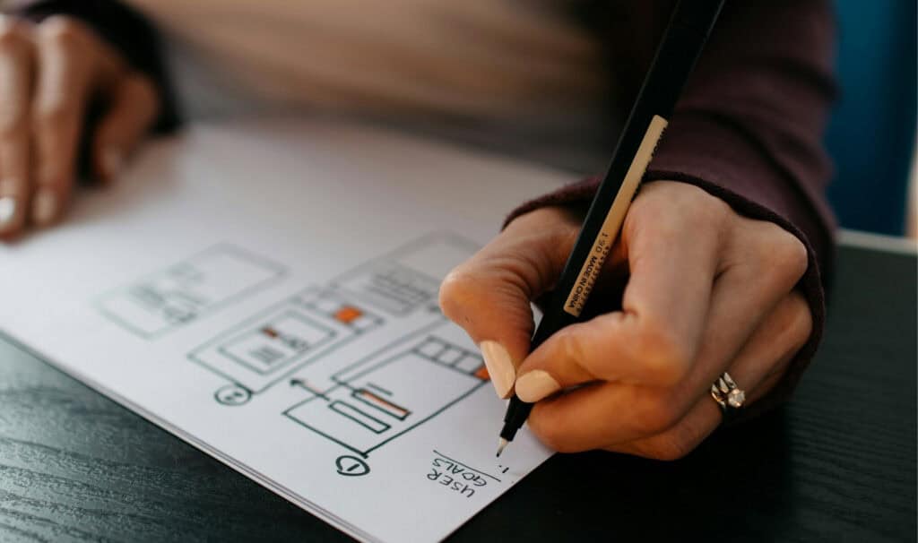 Design planning sketch on paper with a person drawing with a black pen.