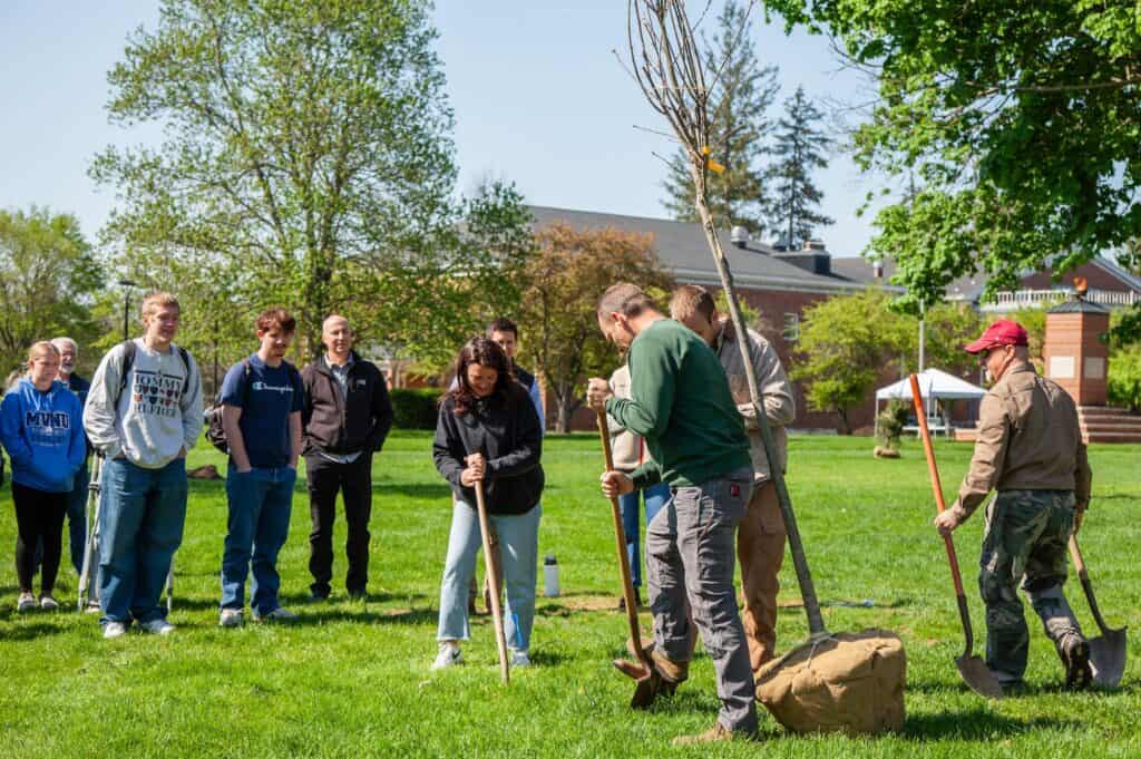 Planting trees with a group of people outdoors on a sunny day.