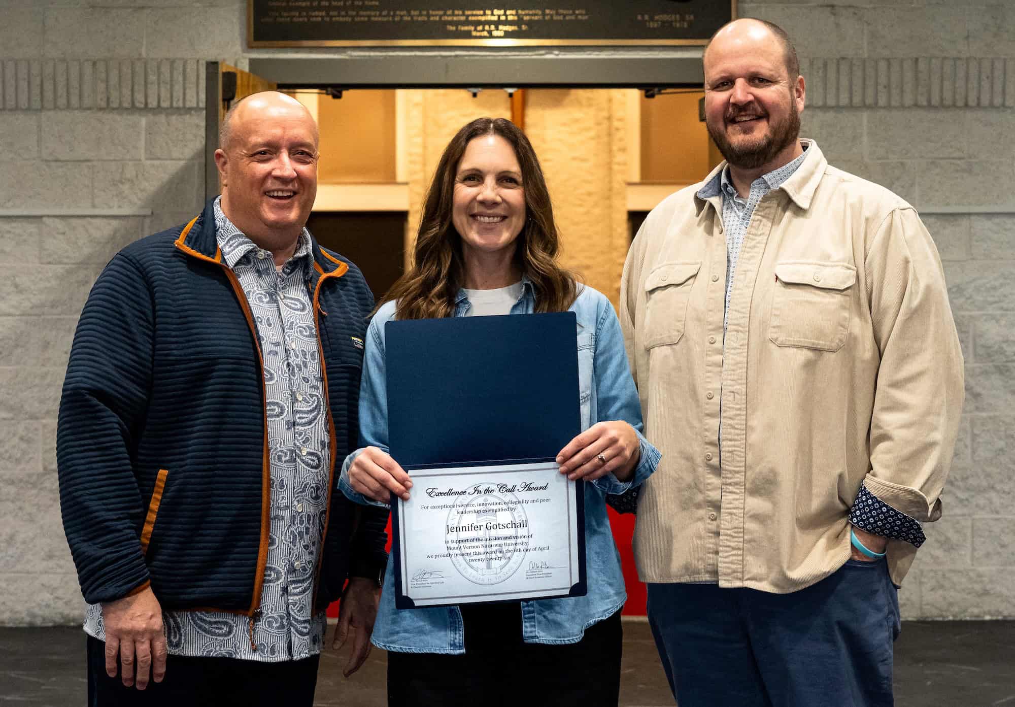Graduation ceremony with three smiling individuals, one holding a diploma, celebrating achievement.