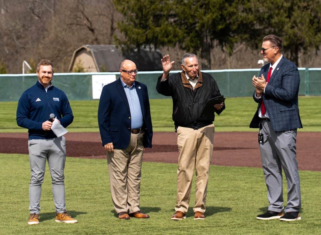 Four men standing on a baseball field during a formal event or ceremony.