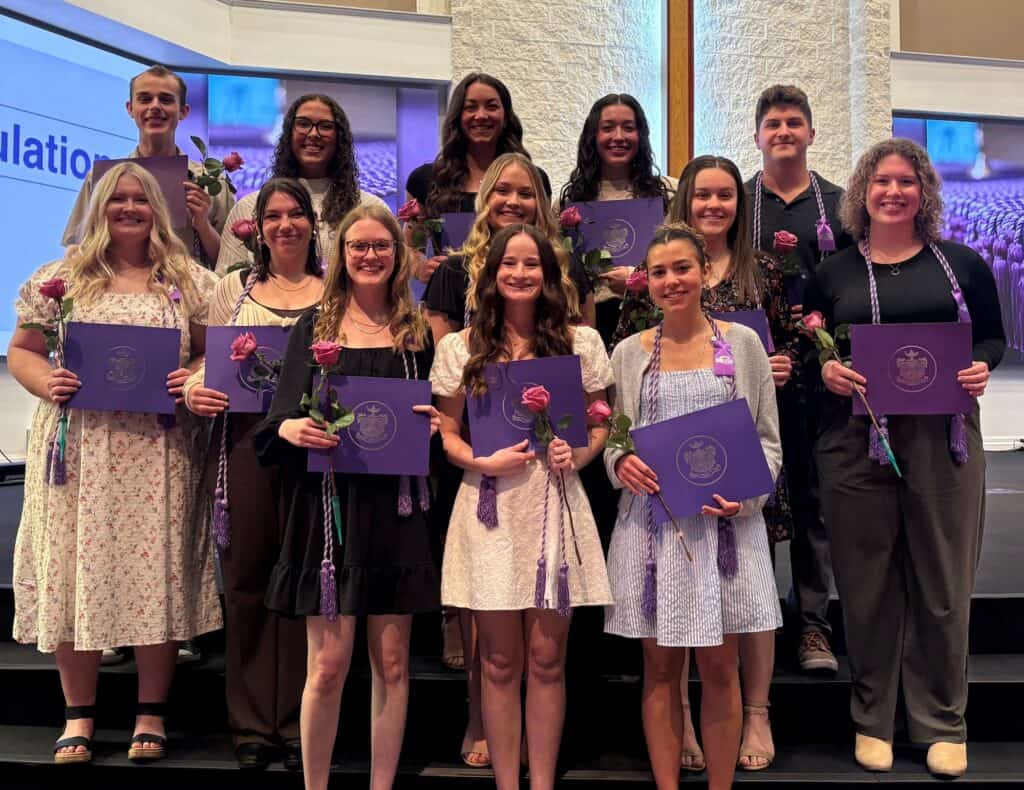 Graduation ceremony with students holding diplomas and flowers, celebrating academic achievement.