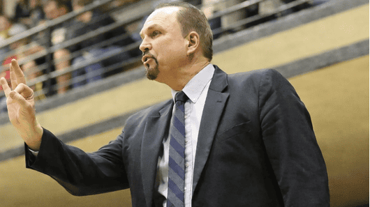 A man in a suit gesturing with his hand during a formal event or meeting.