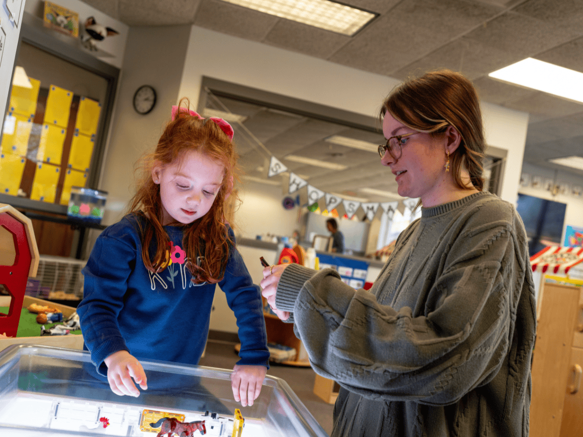 Young girl and woman playing with toys at a classroom table, engaging in educational activity.