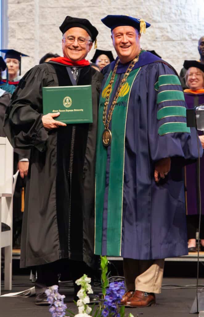Two men in academic gowns and caps smiling at the ceremony.