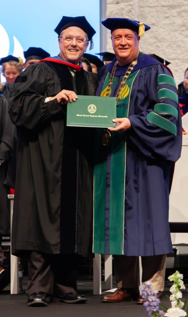Graduation ceremony featuring two men in academic regalia, one holding a diploma, celebrating academ.