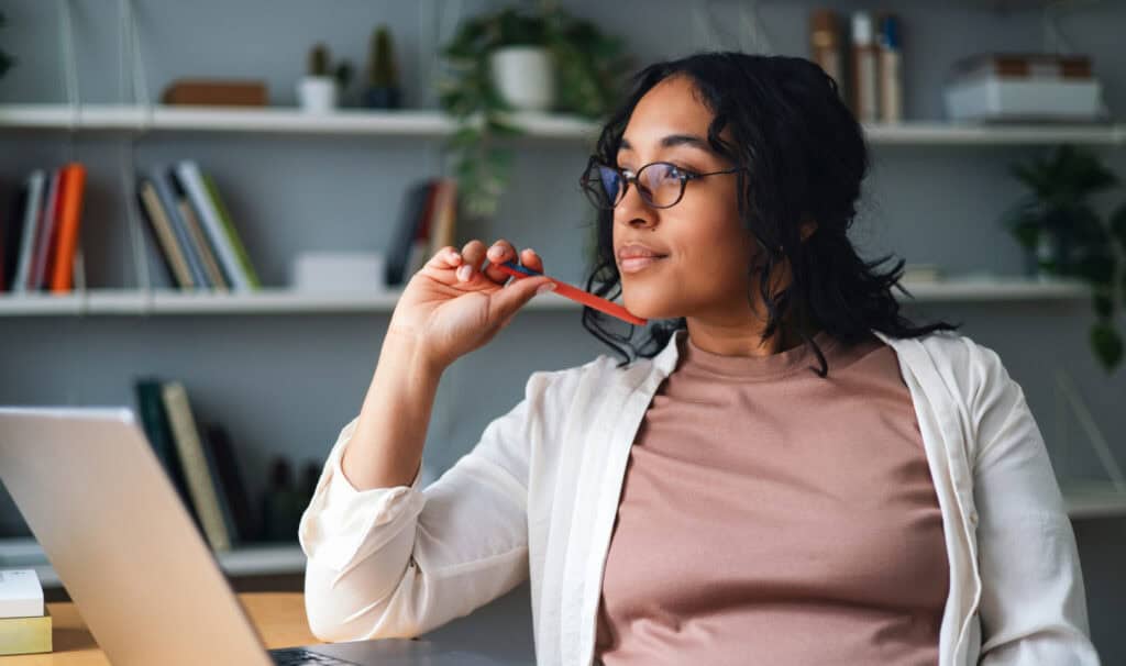 A focused professional woman at her home office desk with a laptop and pencil, illustrating the careful research working adults do when choosing an online degree program that fits their schedule and career goals.