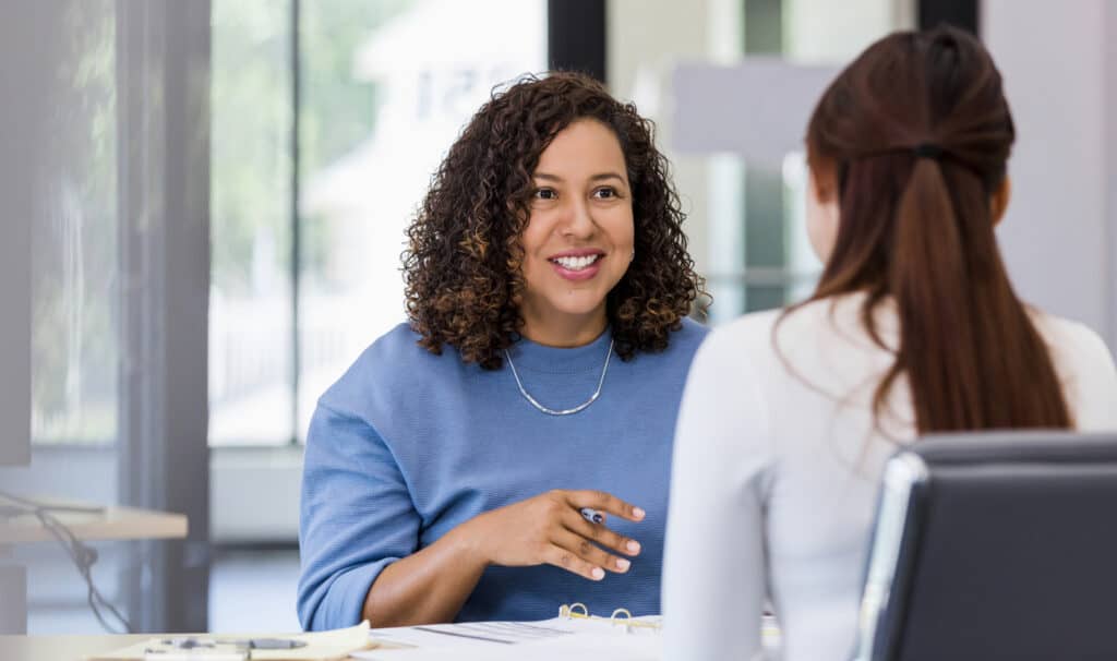 Two female coworkers discussing a project in a modern office, reflecting how an online degree from MVNU can support promotions, career mobility, and increased earning potential.