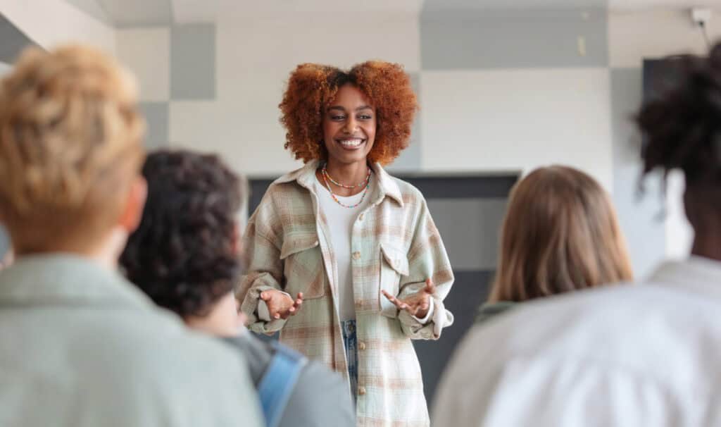 A confident woman addresses a small group in a classroom setting, reflecting how a ministry degree from MVNU Online develops the communication and people-centered leadership skills that translate into any room where influence matters.