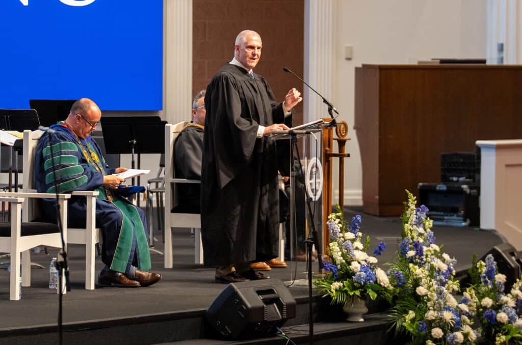 Man in academic gown speaking at graduation ceremony podium.