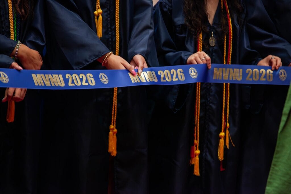 Students in caps and gowns holding a "MMU 2026" ribbon at graduation.