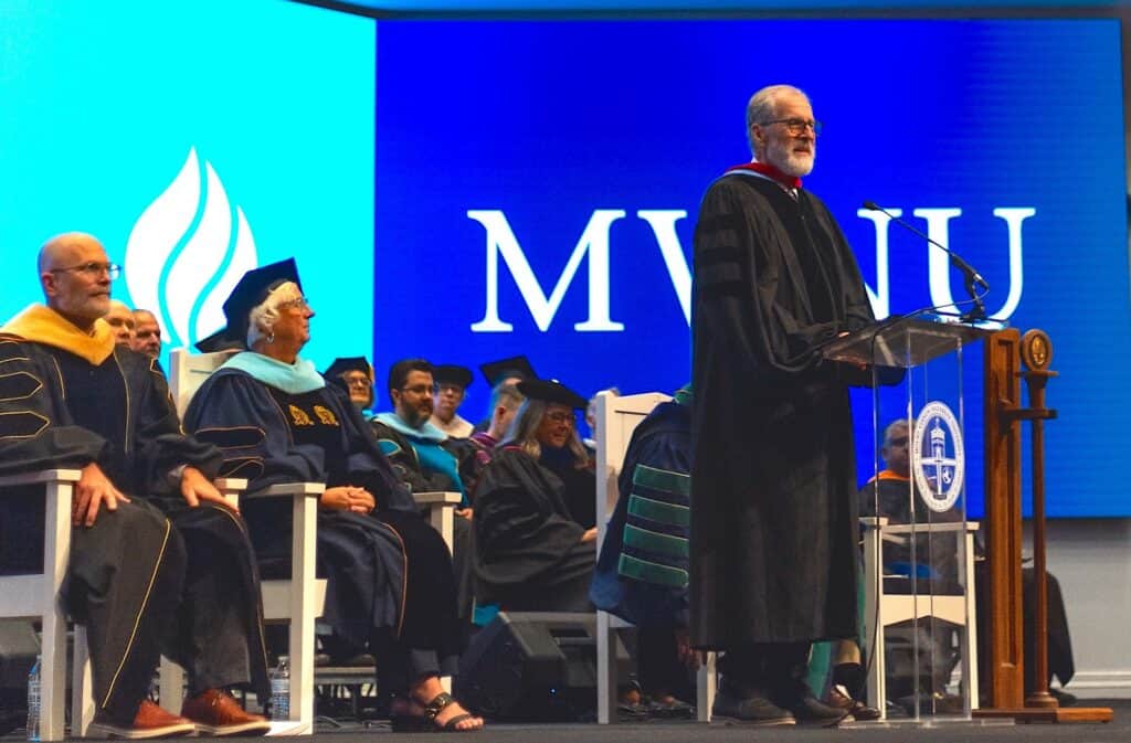 University graduation ceremony with officials and speaker on stage.